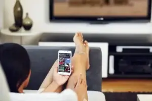woman relaxing on the hotel room couch using their phone as a remote control