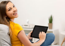 Teenage girl using iPad in living room chair