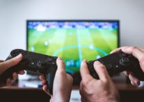 Two people holding Sony Playstation controllers in front of a large television