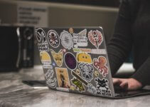 person surfing laptop covered in stickers near microwave oven