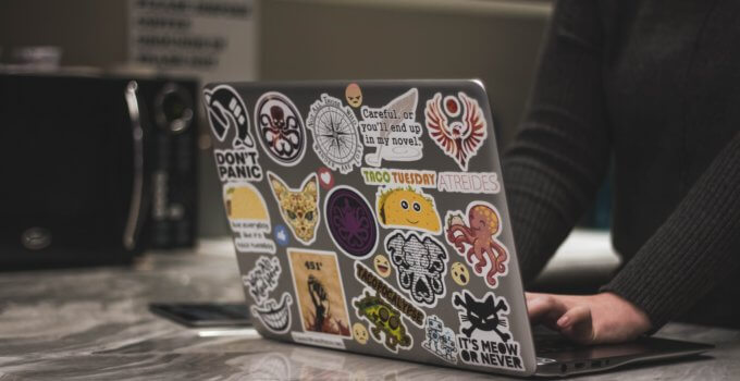 person surfing laptop covered in stickers near microwave oven