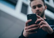 man wearing black sweater using smartphone to monitor his kids