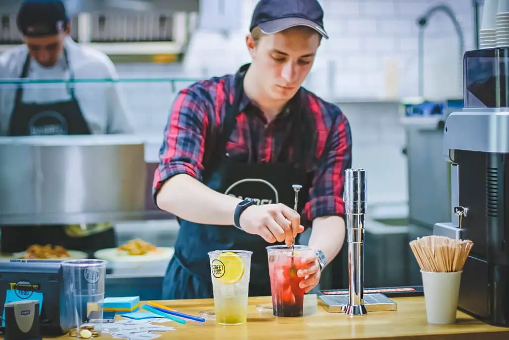 Student working their first job by mixing fruity beverages at the back of a restaurant.