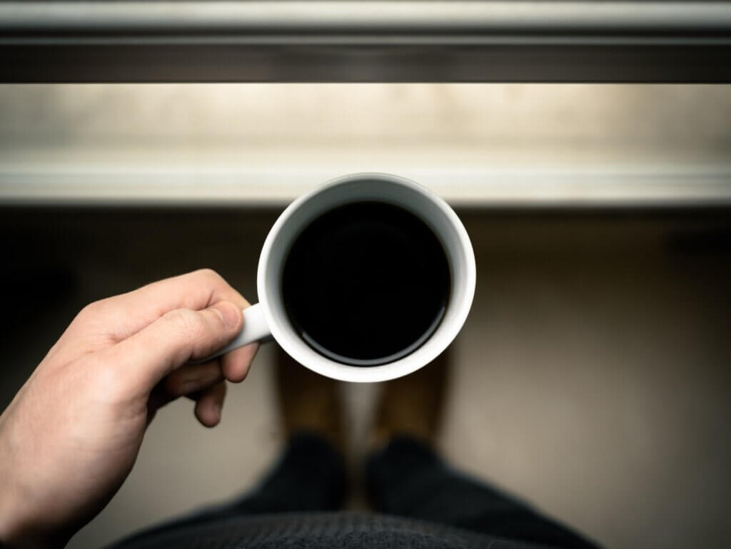 College student holding white ceramic mug filled with black coffee