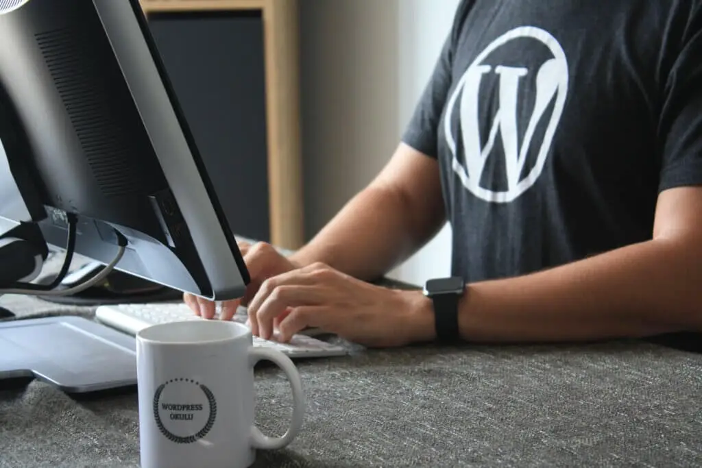 man in black and white WordPress t-shirt using computer to blog