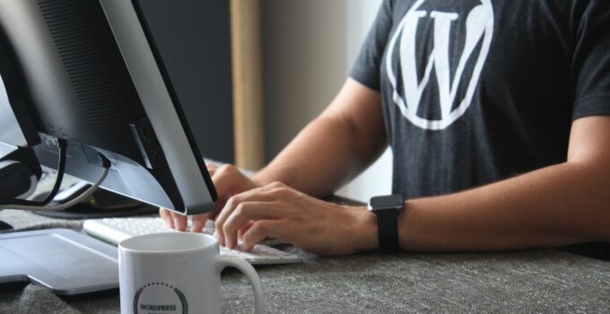 man in black and white WordPress t-shirt using computer to blog
