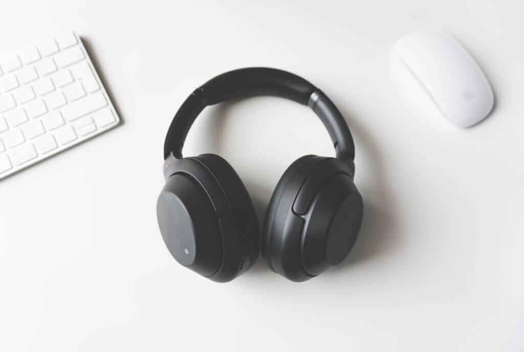 Black wireless headphones between Apple Keyboard and Apple Magic Mouse on white surface