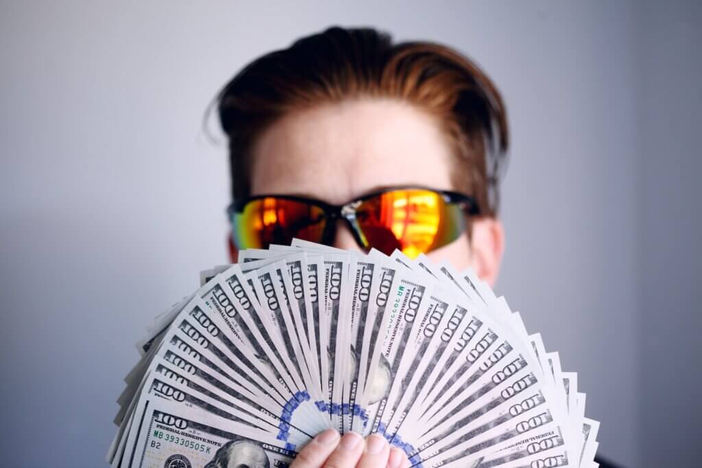 How do free apps make money online? Man in black framed sunglasses holding fan of money - how do free apps make money?